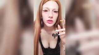 smoking redhead with bright makeup in a black leather dress